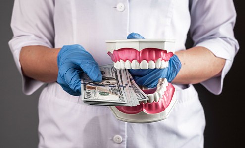 A dentist holding hundred-dollar bills and a model jaw