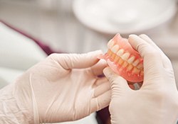 Gloved hands holding two full dentures in a dentist’s office
