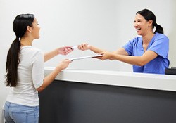 Smiling dental assistant handing patient form