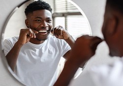 Man smiling while flossing in mirror