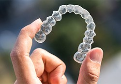 A hand holding a clear Invisalign tray against a blurred background