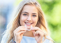 A happy, smiling woman holding an Invisalign tray in front of her
