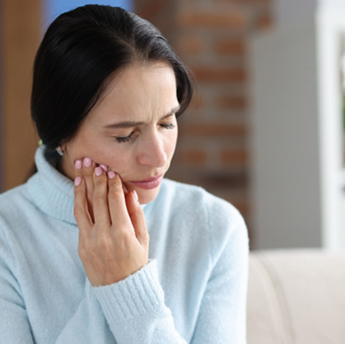 Woman sitting on couch rubbing jaw in pain