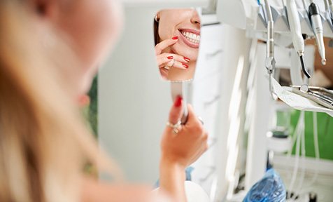 A woman admiring her treated smile with a hand mirror