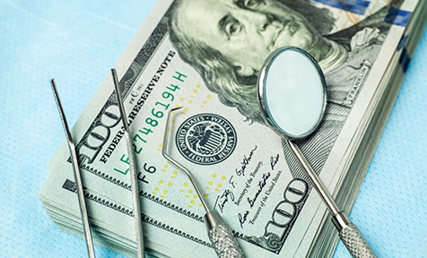 Dental tools laying on a pile of hundred-dollar bills