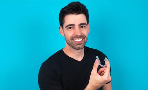 Man in black t-shirt holding Invisalign aligner