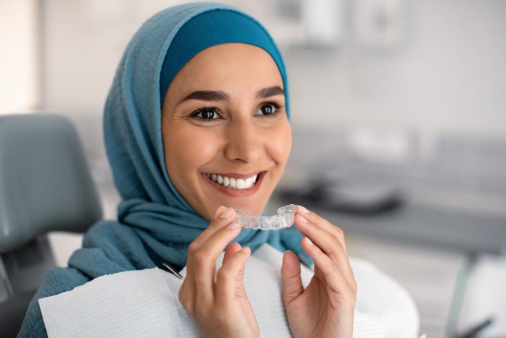 Woman in dental chair smiling while holding Invisalign aligner
